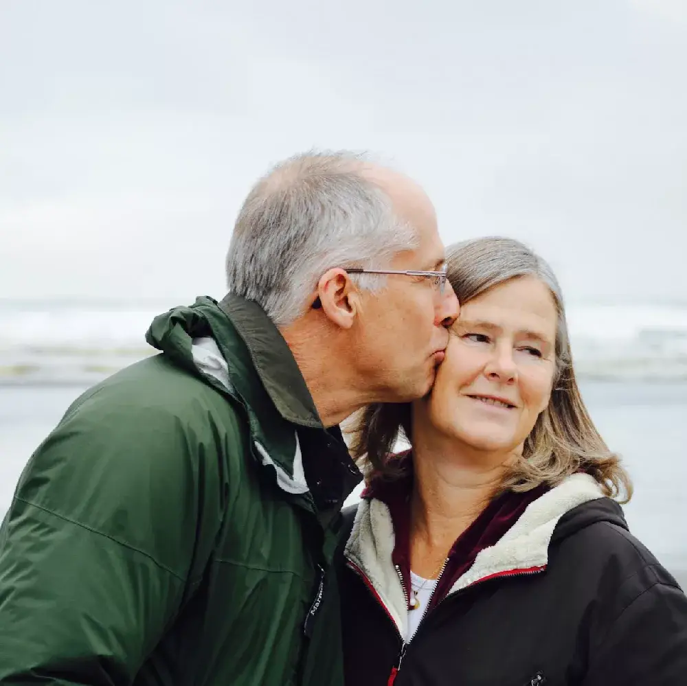 Couple on a beach, man is kissing women's cheek.