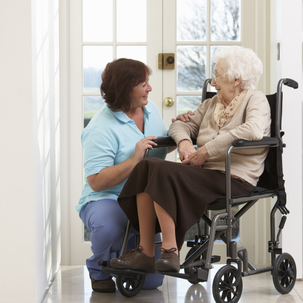 lady carer crouching by lady elderly lady in a wheelchair, both smiling